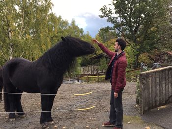 Woman standing by horse against trees