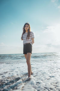 Portrait of young woman standing in sea against sky