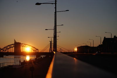 Silhouette bridge over street against sky during sunset