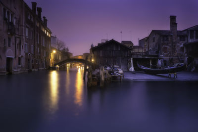 Illuminated buildings by river against sky at night