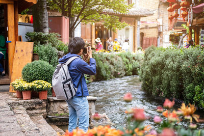 Rear view of woman holding flowering plants against building