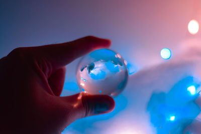 Close-up of hand holding crystal ball against lights