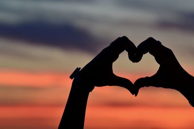 Close-up of silhouette hand holding heart shape against sky during sunset