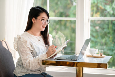 Young woman using mobile phone while sitting on table