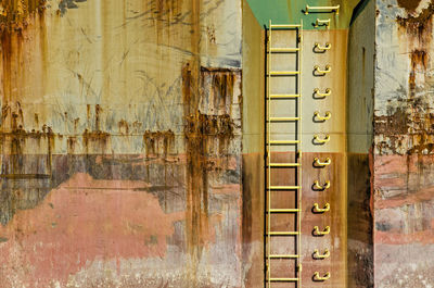 Colorfull section of an old ship's hull with rust, scratches, peeling paint and a ladder