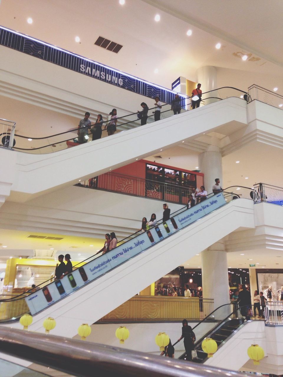 indoors, architecture, built structure, railing, steps and staircases, staircase, steps, ceiling, illuminated, men, low angle view, lifestyles, person, modern, high angle view, shopping mall, walking, incidental people, large group of people