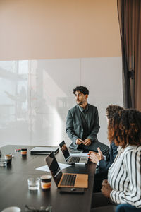 Male entrepreneur sitting on table and discussing with colleagues in board room at office
