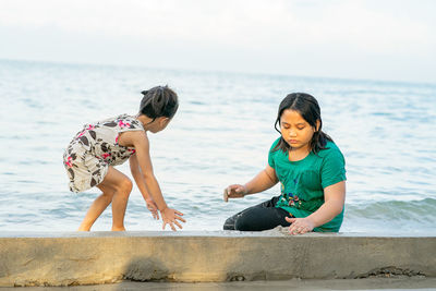 Full length of young woman sitting on rock at beach