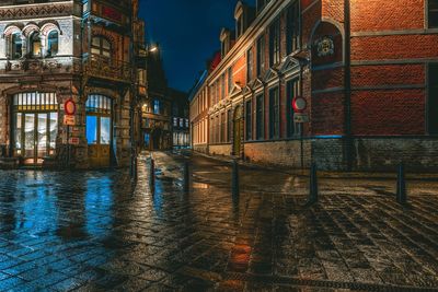 Wet illuminated street amidst buildings in city at night