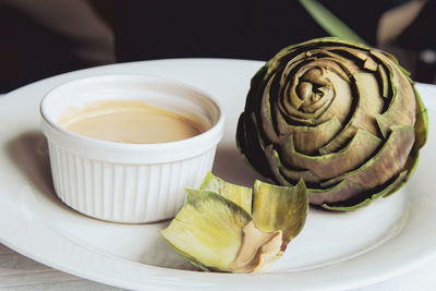 Close-up of steamed artichoke on white plate with dip