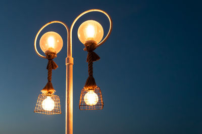 Low angle view of illuminated street light against blue sky