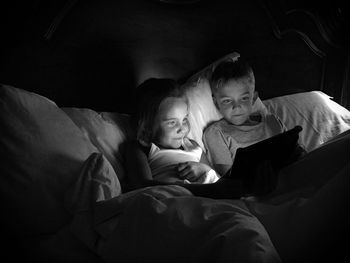 Smiling siblings using digital tablet on bed at home