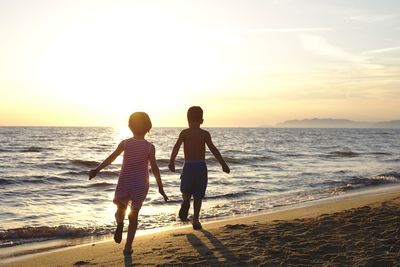 Rear view of men on beach against sky during sunset