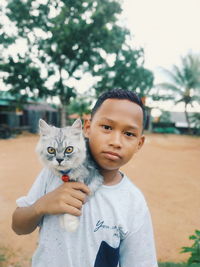 Portrait of boy holding cat on shoulder while standing against trees