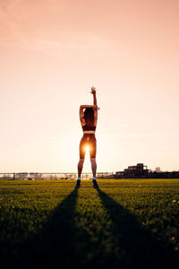 Rear view of man standing on field against sky during sunset