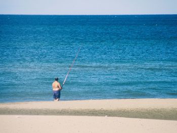 Rear view of man fishing on beach against clear sky
