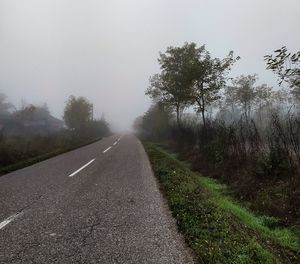 Empty road amidst trees against sky