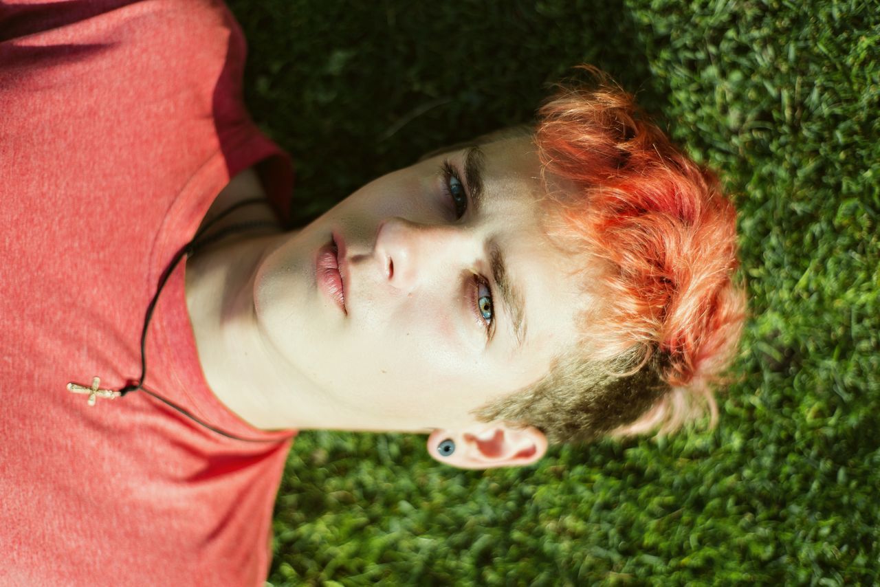 one person, portrait, leisure activity, headshot, child, high angle view, lifestyles, real people, red, lying down, looking at camera, childhood, day, casual clothing, lying on back, young adult, relaxation, front view, hairstyle, beautiful woman, outdoors, contemplation