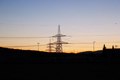 Low angle view of silhouette electricity pylon against sky at sunset