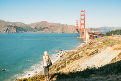 Rear view of woman with backpack looking at golden gate bridge against sky