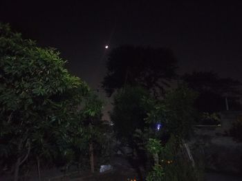 Illuminated street amidst trees against sky at night