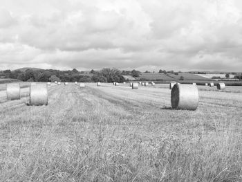 View of hay bales on landscape against cloudy sky