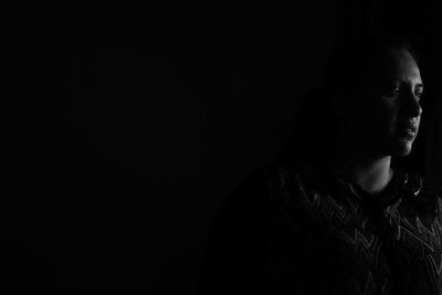 Portrait of young woman looking away against black background