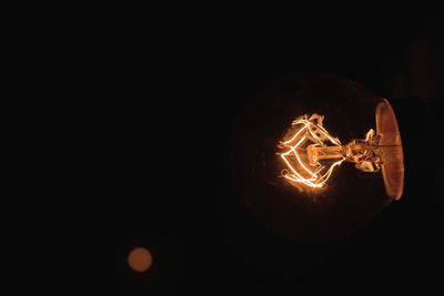 Close-up of illuminated light bulb against black background