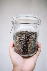 Close-up of hand holding glass jar against white background