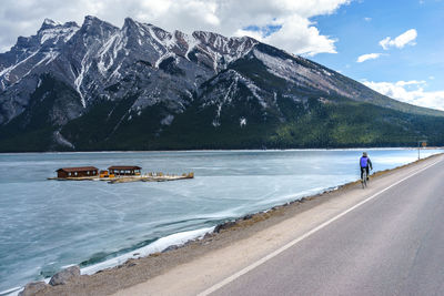 Rear view of man riding bicycle by lake against sky