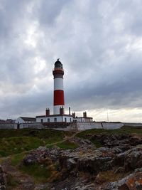 Lighthouse on beach by building against sky