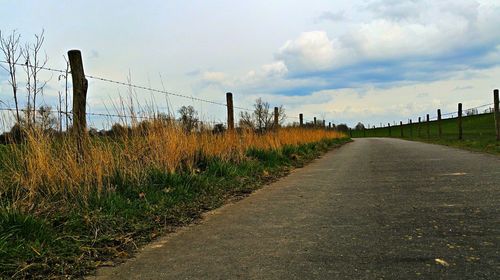 Road passing through field against cloudy sky