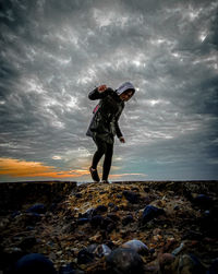 Man standing on rock at beach against sky during sunset