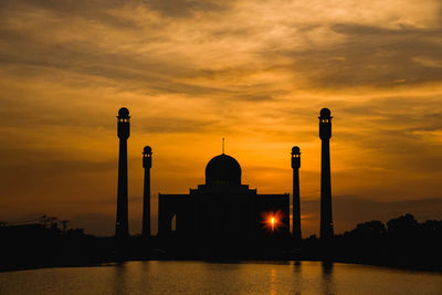 Silhouette mosque by lake against orange sky