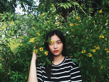 Portrait of beautiful young woman standing against plants