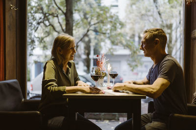 Smiling mature couple looking at each other while having wine at bar