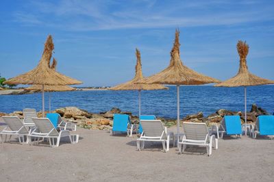 Deck chairs on beach against sky