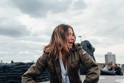 Portrait of young woman standing against sky in city