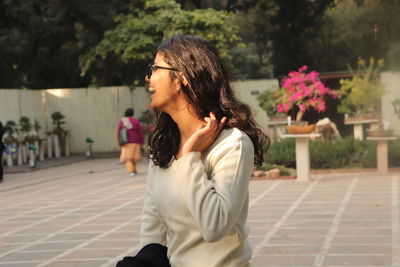 Side view of young woman standing against trees