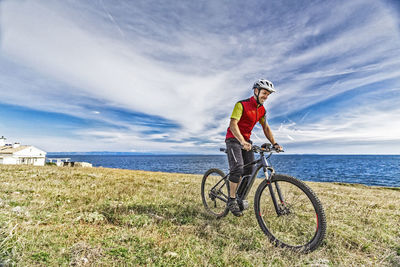 Full length of mountain biker on field against sea