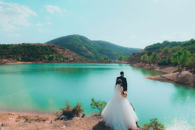 Rear view of couple holding hands while standing by lake