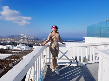 Woman standing by railing in city against sky