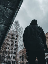 Rear view of man standing by building against sky