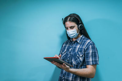 Young man using smart phone while standing against blue wall