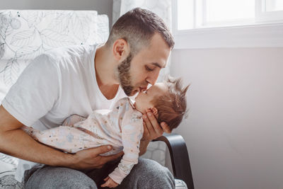 Man kissing daughter while sitting on armchair at home