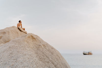 Rear view of naked man sitting on rock