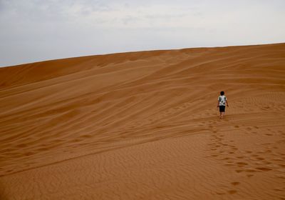 Rear view of boy on sand dune in desert against sky