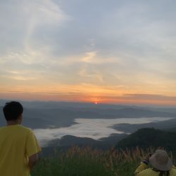 Rear view of man standing on mountain against sky during sunset