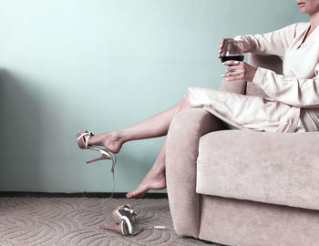 Low section of woman sitting on sofa against wall