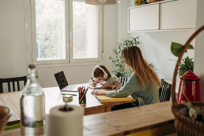 Mother looking at daughter doing homework sitting with laptop at table